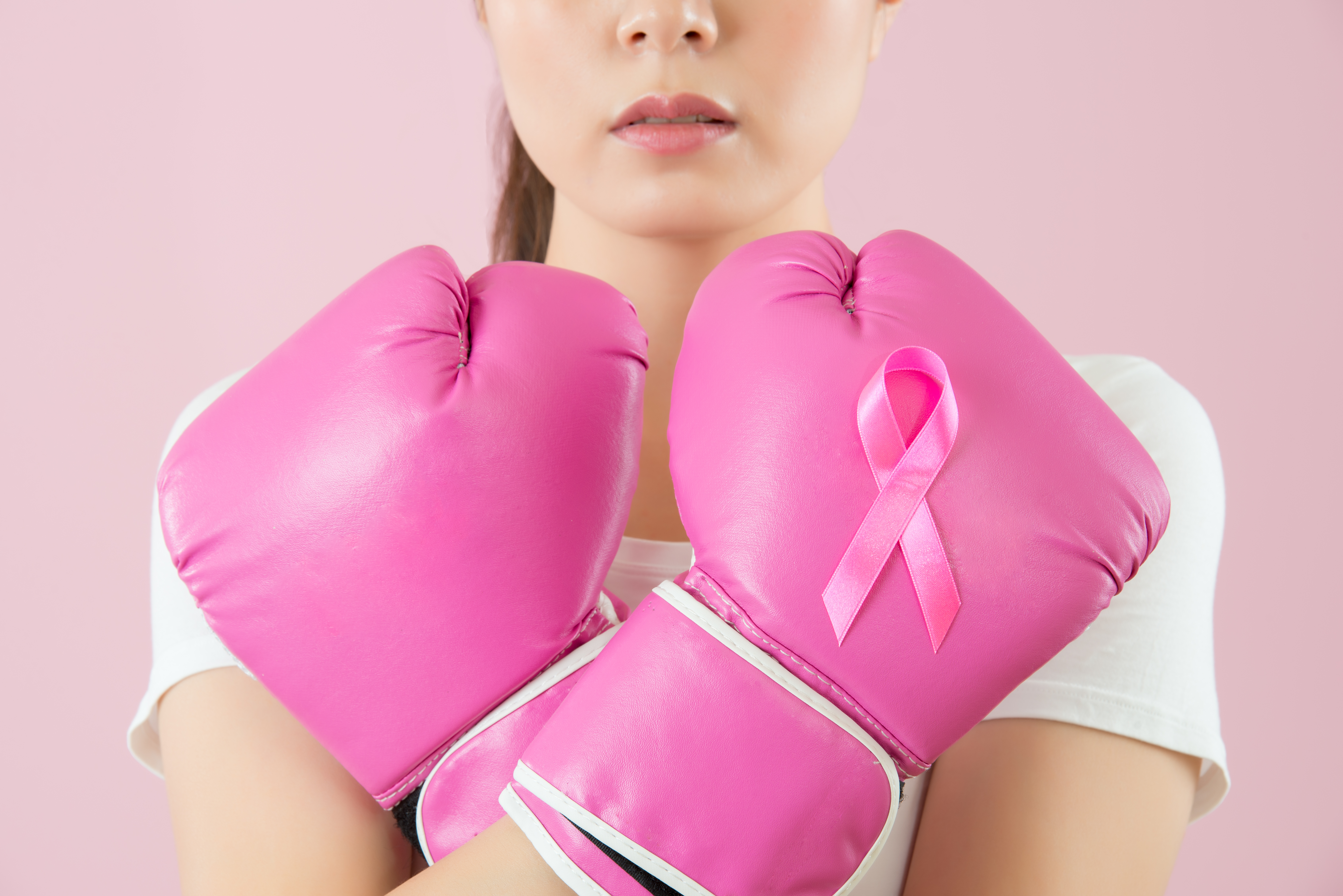 Woman wearing pink boxing gloves with breast cancer awareness ribbon on one.