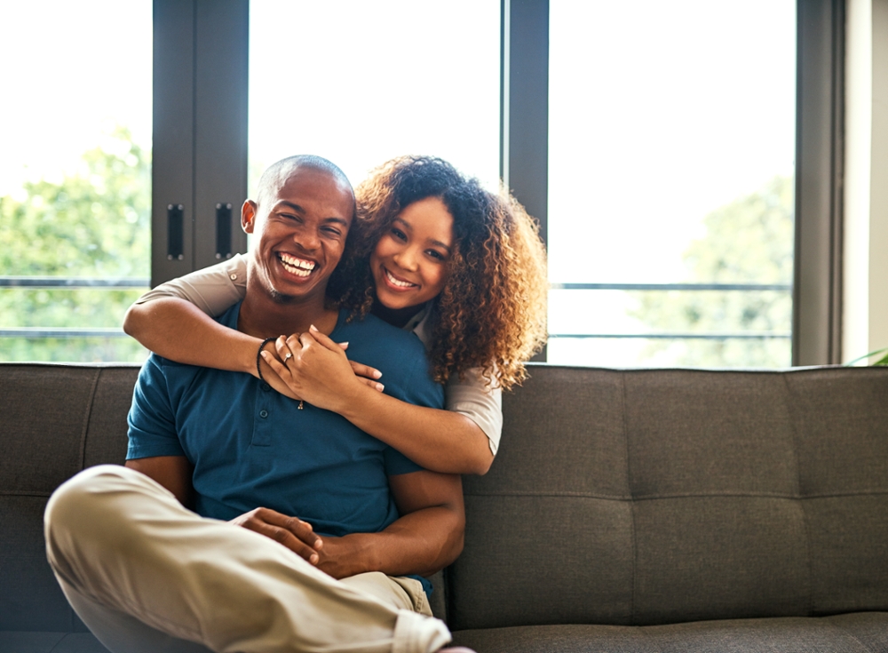 Couple hugging on couch smiling at camera.