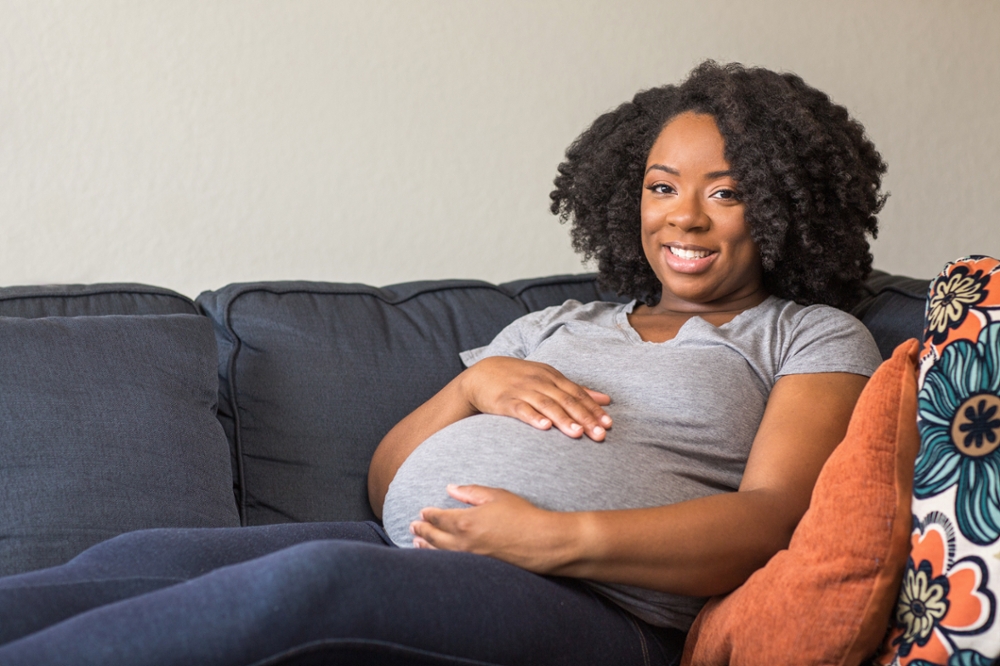 Pregnant woman sitting on couch smiling at camera.