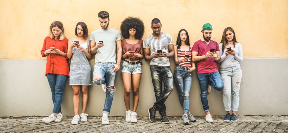 Multiracial friends using smartphone against wall at university college backyard. Stock photo ID:1092747784