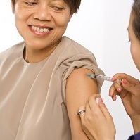 Smiling woman receiving a vaccination shot in her upper arm from a healthcare provider.